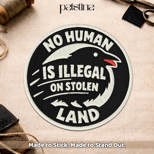 May include: A round, black and white embroidered patch with the text "NO HUMAN IS ILLEGAL ON STOLEN LAND". The patch features a bird design and the text "Made to Stick. Made to Stand Out."