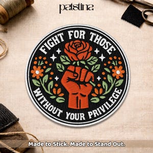 May include: Embroidered patch with the text "FIGHT FOR THOSE WITHOUT YOUR PRIVILEGE". The design features a raised fist, a rose, and floral elements in orange, green, and white on a black background. The patch is round.