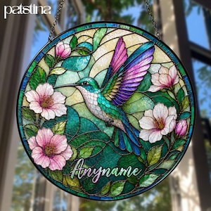 May include: Round stained glass window featuring a hummingbird with teal, purple, and white feathers, surrounded by pink and white flowers and green leaves. The text "Anymame" is written in cursive. The brand name "patsina" is at the top.