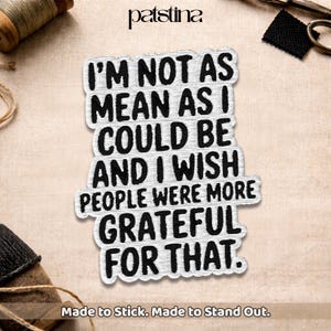 May include: A white and black embroidered patch with the text "I'M NOT AS MEAN AS I COULD BE AND I WISH PEOPLE WERE MORE GRATEFUL FOR THAT." The patch is rectangular and has a distressed look. The patch is made to stick.