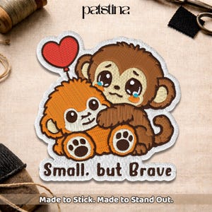 May include: Embroidered patch featuring two cartoon monkeys hugging, one brown and one orange, with a red heart balloon. The patch has the text "Small, but Brave" and "Made to Stick. Made to Stand Out."