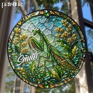 May include: A circular stained glass suncatcher featuring a detailed green praying mantis surrounded by yellow flowers and green foliage. The piece has a textured, iridescent background and the name Smith written in white script across the lower left.