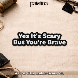 May include: Black and white embroidered patch with the text "Yes It's Scary But You're Brave". The patch is on a beige fabric background. The brand name "patstina" is at the top.