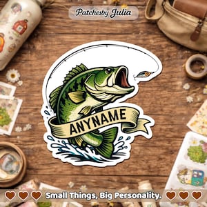 May include: A sticker featuring a green and white bass fish with an open mouth, a fishing lure, and a banner that says "ANYNAME". The sticker is on a wooden surface. The text "Small Things, Big Personality" is at the bottom.