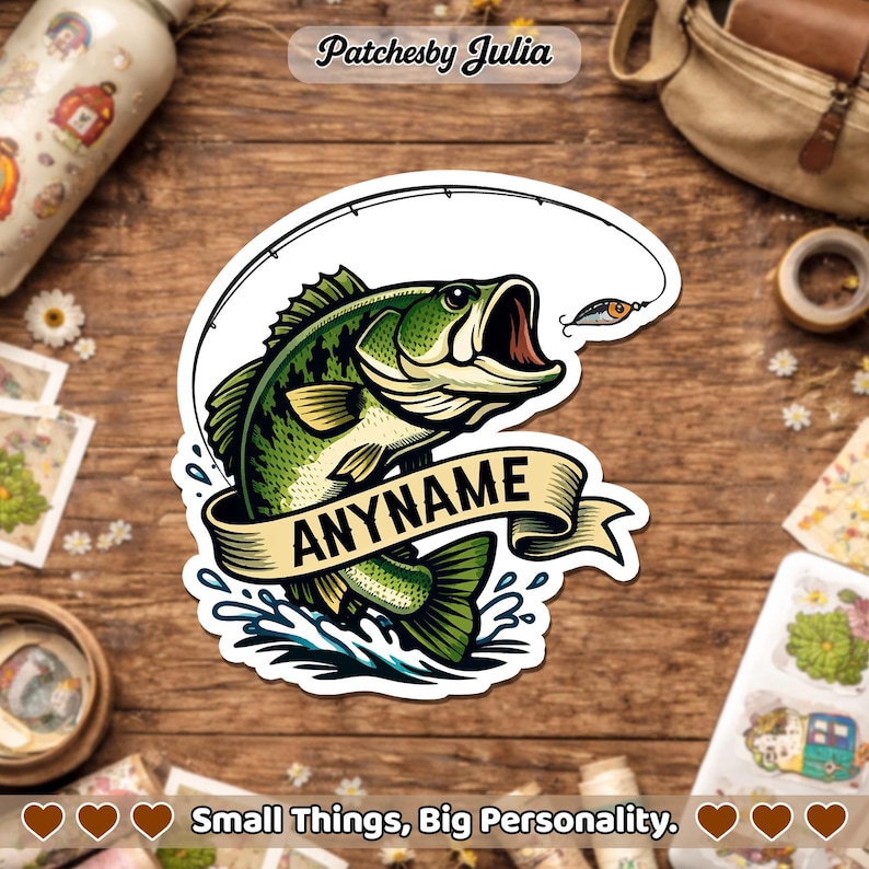 May include: A sticker featuring a green and white bass fish with an open mouth, a fishing lure, and a banner that says "ANYNAME". The sticker is on a wooden surface. The text "Small Things, Big Personality" is at the bottom.