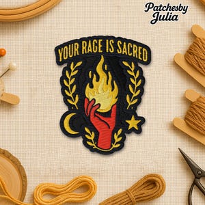 May include: Embroidered patch with the text "YOUR RAGE IS SACRED". The patch features a black background with a red hand holding a flame, surrounded by gold laurel leaves, a crescent moon, and a star. The patch is made by Patchesby Julia.