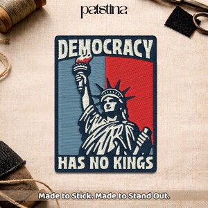 May include: Embroidered patch featuring the Statue of Liberty with the words "DEMOCRACY HAS NO KINGS." The design is set against a blue and red background. The patch is rectangular and has the text "Made to Stick. Made to Stand Out."