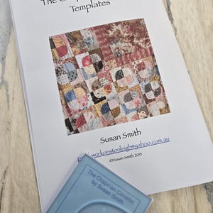 May include: A white booklet with the title "The Chapman Coverlet Templates" and a colorful quilt pattern image. The booklet includes the name "Susan Smith" and an email address. A blue plastic template with the text "The Chapman Coverlet by Susan Smith" is in the foreground.