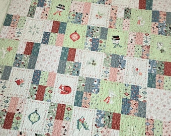 Puede incluir: Un edredón de retazos con temática navideña. El edredón presenta cuadrados en tonos de blanco, verde, rojo y azul. Algunos cuadrados tienen imágenes con temas navideños como muñecos de nieve, adornos y acebo. El edredón está hecho de tela suave.