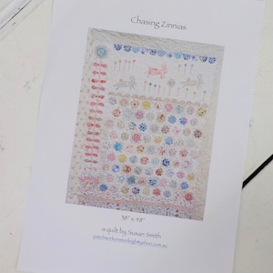 May include: A quilt pattern featuring a colorful floral design with a white background. The quilt is 38 inches by 48 inches and is titled "Chasing Zinnias". The pattern is by Susan Smith and the website patchworkonstleigh@yahoo.com.au is listed.