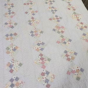 May include: A white quilt with a diamond pattern made of patchwork squares in various floral prints. The quilt is made of cotton fabric and has a subtle texture.