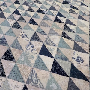 Könnte beinhalten: Eine Decke aus blauem, weißem und grauem Stoff mit einem geometrischen Muster aus Dreiecken.