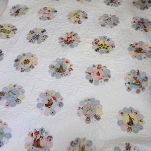 May include: A white quilt with a pink border. The quilt is made up of a series of circular patterns, each featuring a different animal and floral design. The animals include rabbits, birds, squirrels, and foxes.