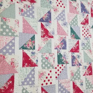 Peut inclure: Une courtepointe en patchwork avec un fond blanc et une variété de triangles colorés. Les triangles sont faits de différents tissus avec des motifs floraux, des pois et des rayures. La courtepointe est faite de différentes couleurs, notamment le rouge, le rose, le vert, le bleu et le blanc.