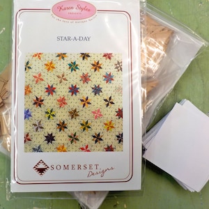 May include: A quilting pattern titled "Star-A-Day" by Karen Styles for Somerset Designs. The pattern features a quilt design with a variety of colorful stars on a white background.