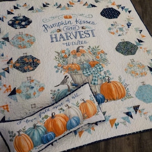 May include: A white quilt with a blue and orange patchwork design. The quilt features a pillow with the text "I love fall most of all..." and a larger design with the text "Pumpkin Kisses (and) HARVEST Wishes".