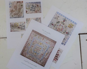 May include: A quilt pattern called "The Storyteller" by Susan Smith. The pattern is for a quilt with 87 squares. The quilt is made of white fabric with blue and pink floral embroidery. The pattern is available for purchase on the website patchworkandquiltingbythesea.com.au.