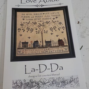 May include: A cross-stitch pattern featuring a tree with houses and the text "In our home let love abide and bless all those who step inside". The pattern is titled "Love Abide" and is from the company "La-D-Da designs for counted thread".