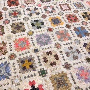 May include: A quilt with a white background and a patchwork design of various floral patterns in shades of pink, blue, green, brown, and yellow. The quilt is made up of squares with a diamond pattern border.