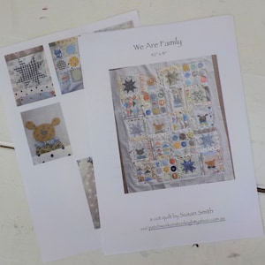 May include: A cot quilt pattern titled "We Are Family" measuring 42 inches by 51 inches. The pattern features a patchwork design with a variety of colors and fabrics, including blue, yellow, white, and red. The quilt is made up of squares and rectangles, and it includes a variety of designs, such as stars, circles, and animals. The pattern is designed by Susan Smith and is available for purchase online.