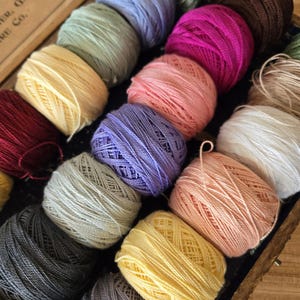 May include: A collection of colorful yarn balls in a wooden box. The yarn is arranged in a circular pattern, with each ball touching the next. The colors of the yarn include red, pink, purple, blue, green, yellow, and white.
