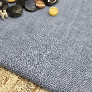 May include: A collection of assorted buttons in various colors and materials, including black, white, brown, and yellow. The buttons are arranged on a light blue fabric background.