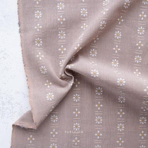 May include: Close-up of a beige fabric with a repeating floral pattern. White daisy-like flowers with yellow centers are arranged in vertical rows. The fabric has a raw edge and the word "FABLEISM" is printed on the fabric.