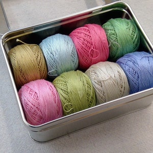 May include: A metal tin filled with eight balls of embroidery floss in various pastel colors, including green, blue, pink, and beige.