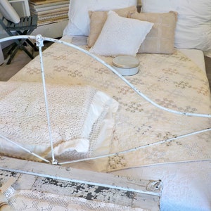May include: A white iron bed frame with a white crocheted bedspread and white pillows. The bed is decorated with lace and a small round tin box.
