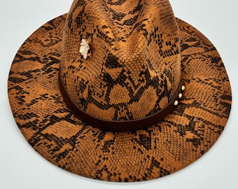 Damesfedora met smalle rand en slangenprint – een neutrale, opvallende hoed met gouden bijenaccenten