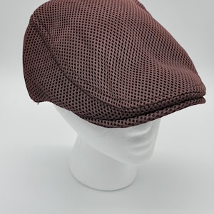May include: A brown flat cap constructed from a breathable mesh fabric. The hat features a rounded crown and a short, stiff brim at the front, showcasing a consistent grid-like texture throughout the entire exterior surface of the headwear.