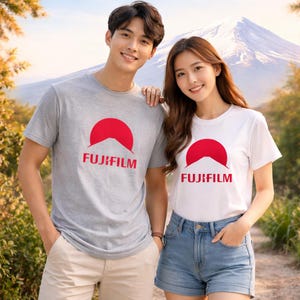 Puede incluir: Dos personas con camisetas grises y blancas con un gráfico rojo de montaña y sol, y la palabra "FUJIFILM" en rojo. El fondo presenta una montaña y árboles.