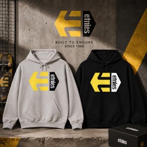 Könnte beinhalten: Ein hellgrauer Kapuzenpullover und ein schwarzer Kapuzenpullover, beide mit einem gelb-schwarzen Etnies-Logo auf der Brust. Das Logo besteht aus einem gelben, pfeilförmigen E und dem Schriftzug etnies. Jeder Pullover hat eine Kapuze mit Kordelzug.