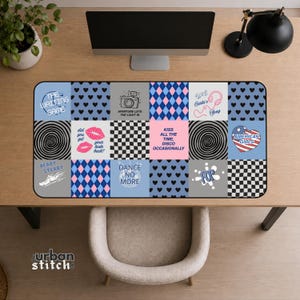 Può includere: Un tappetino da scrivania rettangolare con una griglia di venti quadrati con motivi e testi diversi. I disegni includono cuori neri, motivi a rombi blu, scacchi bianchi e neri, labbra rosa, una fotocamera, una palla da discoteca e vari testi.