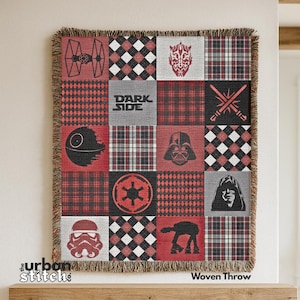 May include: Woven throw blanket with a patchwork design. The blanket features Star Wars-themed graphics in red, black, and white, including Darth Vader, the Death Star, and the text "DARK SIDE". The fringe is a neutral tan colour.