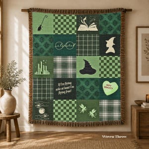 May include: A green woven throw blanket featuring a patchwork design with various patterns and icons including a broom, an open book, a witch hat, a city skyline, and the text If I'm flying solo at least I'm flying free and Defy Gravity.