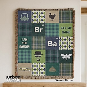 Può includere: Coperta tessuta con un design patchwork con quadrati con varie grafiche e testo. I quadrati includono una maschera antigas, un pollo e le parole "I AM THE DANGER" e "SAY MY NAME". La coperta ha un bordo sfrangiato.