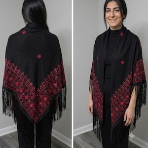 May include: A black triangular shawl featuring intricate red floral embroidery along the edges and scattered across the fabric. The shawl is finished with long black fringe trim along the bottom borders, creating a textured and layered appearance.