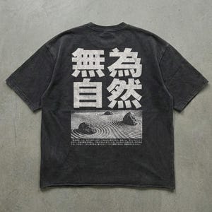 May include: A charcoal gray short-sleeve t-shirt featuring large white Japanese characters at the top, followed by a graphic of a raked sand zen garden with stones, and a block of small Japanese text printed at the bottom of the back design.