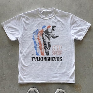 May include: A white short-sleeve t-shirt featuring a graphic of a person in a suit in blue, orange, and black. The text reads STOP MAKING SENSE, /84, and TVLKINGHEVDS. The design is centered on the chest of the shirt, which has a crew neckline.