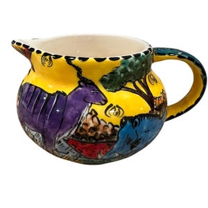 May include: A hand-painted ceramic pitcher with a yellow background and a curved handle. The pitcher features a purple animal, a blue animal, and a tree design. The rim and handle are accented with black and green details.