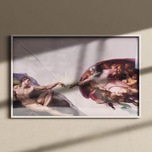Könnte beinhalten: Gerahmter Druck von Michelangelos 'Erschaffung Adams' an einer Wand. Das Kunstwerk zeigt zwei Figuren mit ausgestreckten Armen, die sich fast berühren. Der Druck ist in einem weißen Rahmen, die Wand ist neutralfarben.