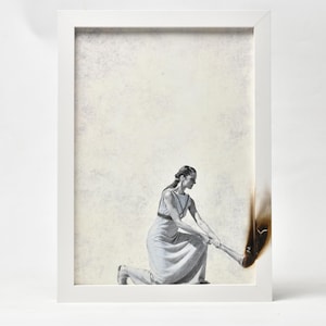 Könnte beinhalten: Gerahmtes Kunstwerk mit einer Graustufen-Illustration einer knienden Person, die einen brennenden Gegenstand hält. Die Person trägt ein langes Kleid. Das Kunstwerk befindet sich in einem weißen Rahmen mit hellem beigen Hintergrund.