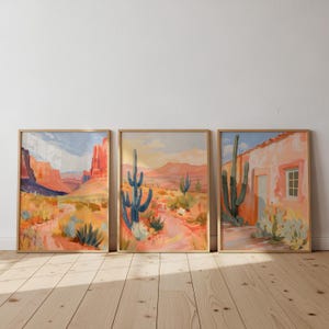 以下が含まれることがあります： 砂漠の風景を描いた3つの額入り風景画。 このアートワークは、サボテン、山、建物などの描写で、オレンジ、青、黄色のカラーパレットを使用しています。 フレームは薄茶色です。
