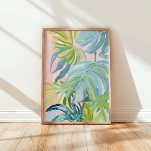 Può includere: Una stampa artistica incorniciata con grandi foglie tropicali stilizzate in tonalità di blu, verde e giallo su uno sfondo rosa tenue. L'opera d'arte è racchiusa in una cornice di legno naturale, creando un'estetica vibrante e rinfrescante.