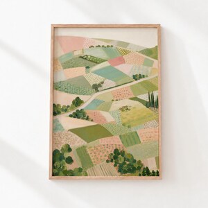 May include: A framed wall art print featuring a landscape painting of rolling hills divided into patchwork fields of soft pink, sage green, cream, and muted yellow. The scene includes small clusters of dark green trees and a winding path.