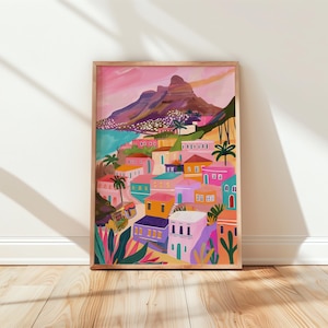 Peut inclure: Une impression d'art encadrée représentant une ville côtière colorée au pied d'une chaîne de montagnes. L'œuvre utilise des couleurs vives comme le rose, l'orange, le bleu et le vert, avec des palmiers et des bâtiments. L'impression est dans un cadre en bois.