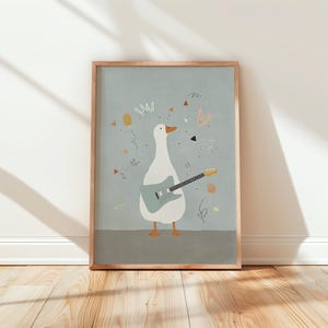 Könnte beinhalten: Ein gerahmter Kunstdruck mit einer skurrilen Illustration einer weißen Gans, die eine blaue Gitarre spielt. Die Gans hat orangefarbene Füße und einen Schnabel, vor einem hellblauen Hintergrund mit Konfetti und abstrakten Formen. Der Rahmen ist hellbraun.