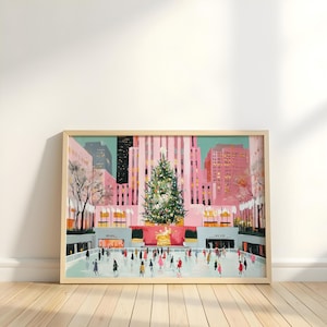 Puede incluir: Una impresión enmarcada que representa una escena invernal con un gran árbol de Navidad frente a un edificio rosa. La gente patina sobre hielo en una pista en primer plano. La obra de arte está en un marco de madera clara y se exhibe en un suelo de madera.