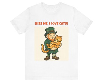 May include: White t-shirt featuring a cartoon leprechaun holding an orange tabby cat. The leprechaun is wearing a green hat and coat. The text "KISS ME, I LOVE CATS!" is printed in orange above the illustration. A fun, St. Patrick's Day themed tee.